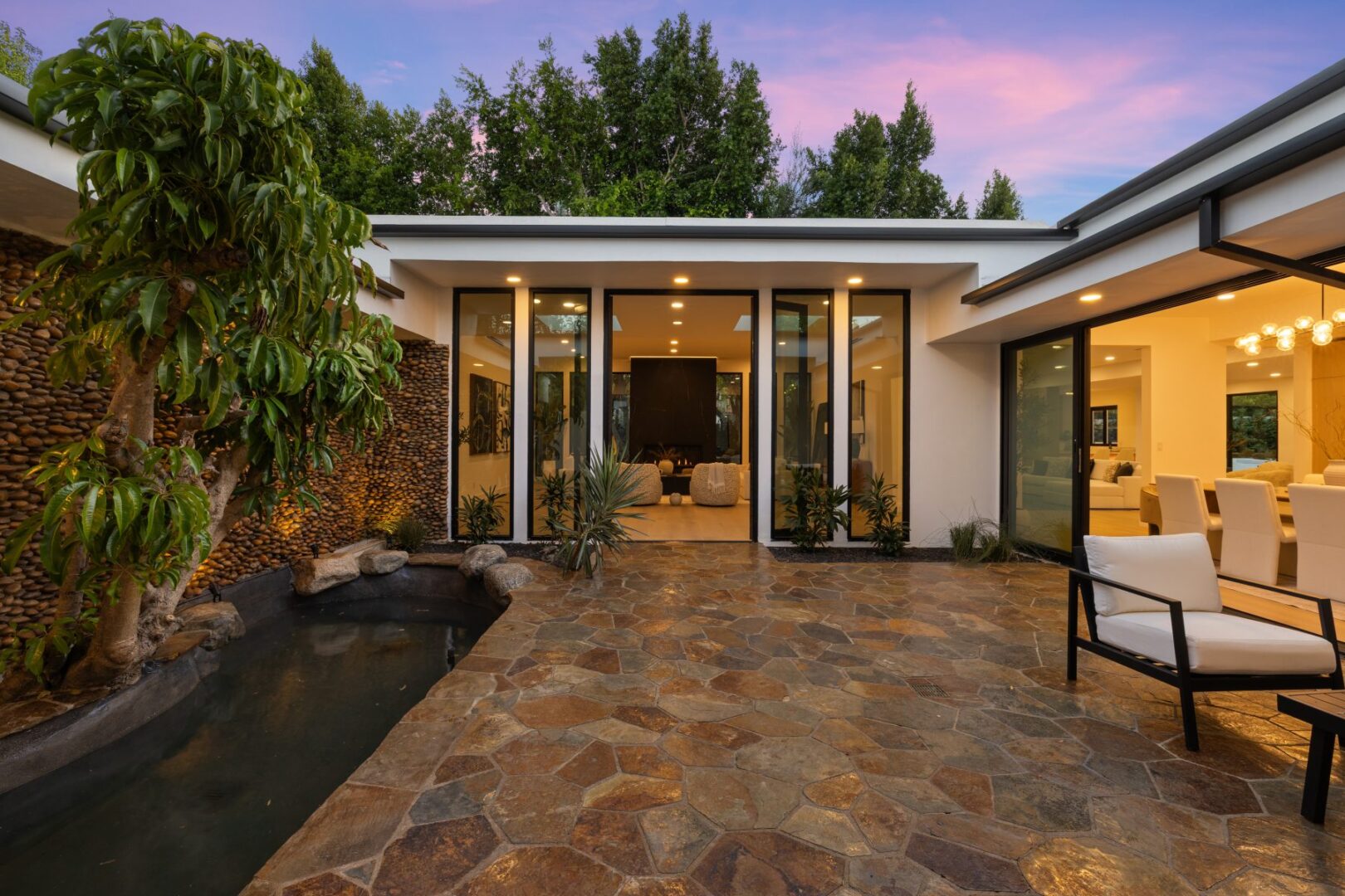 Stone courtyard with a small pond, planting, and broad glass doors connecting to the interior.