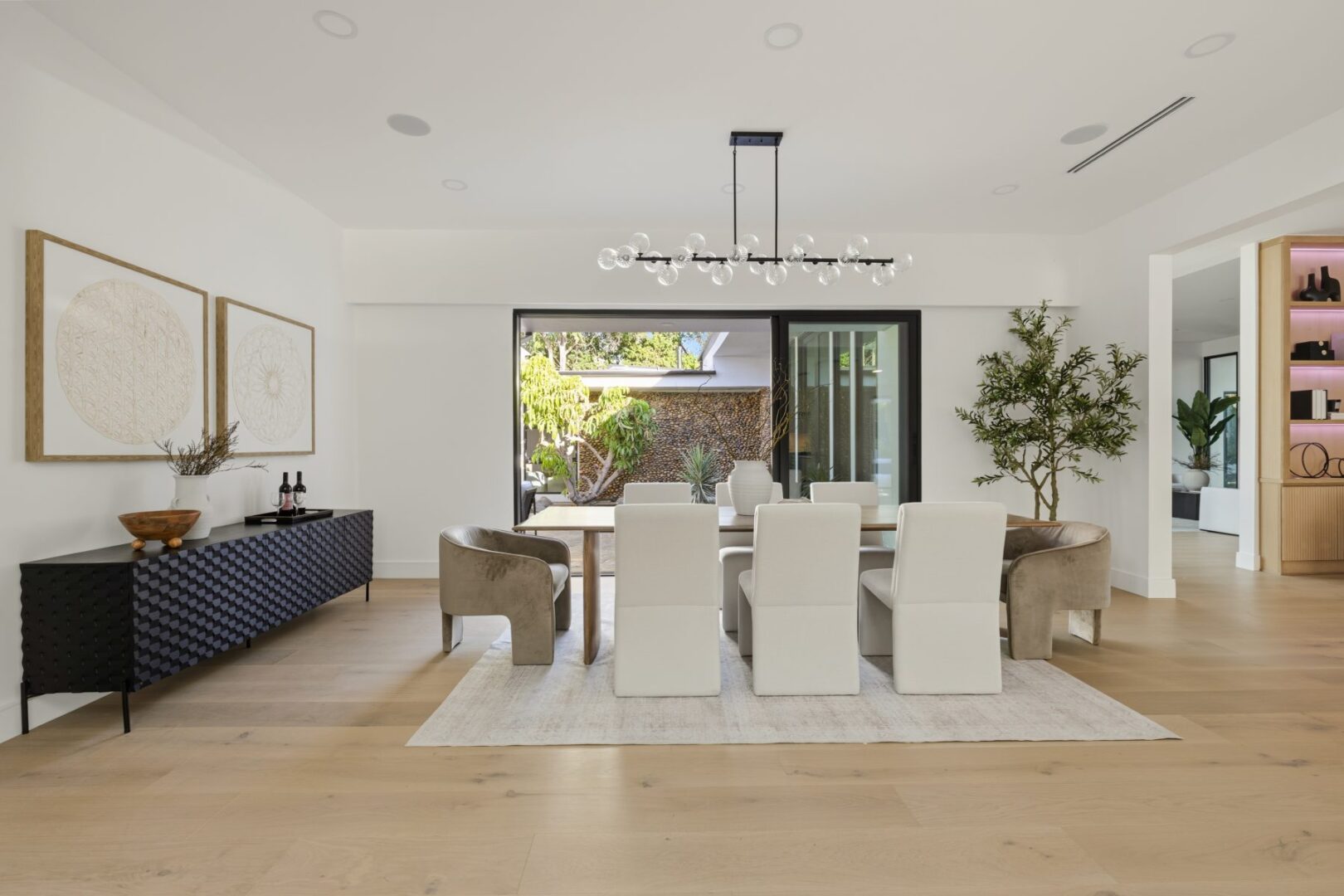 Dining area with a long table, upholstered chairs, sideboard, and sliding doors opening to the patio.