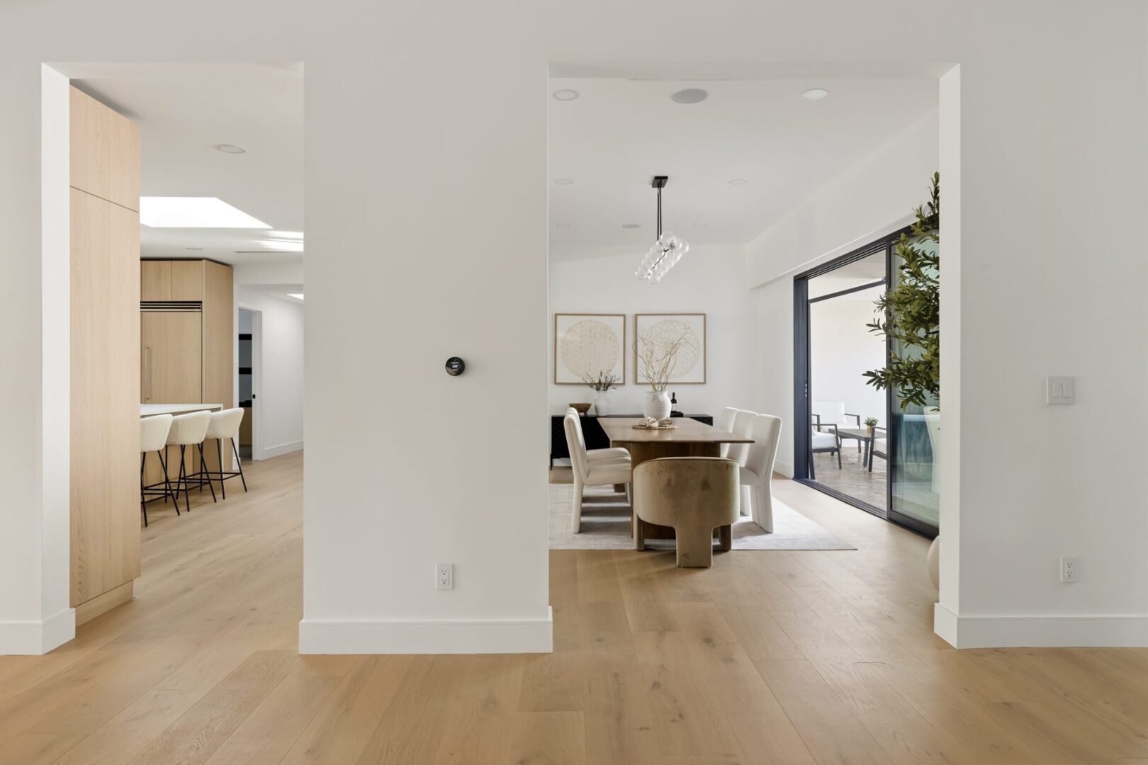 Dining room seen through a wide opening, with a table, upholstered chairs, and sliding doors to the patio.