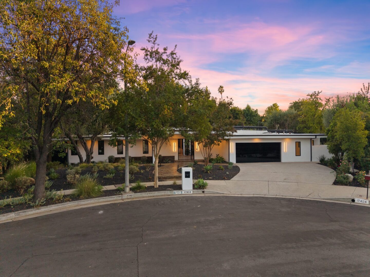 Single-story home with a broad driveway, attached garage, landscaped entry, and mature trees.