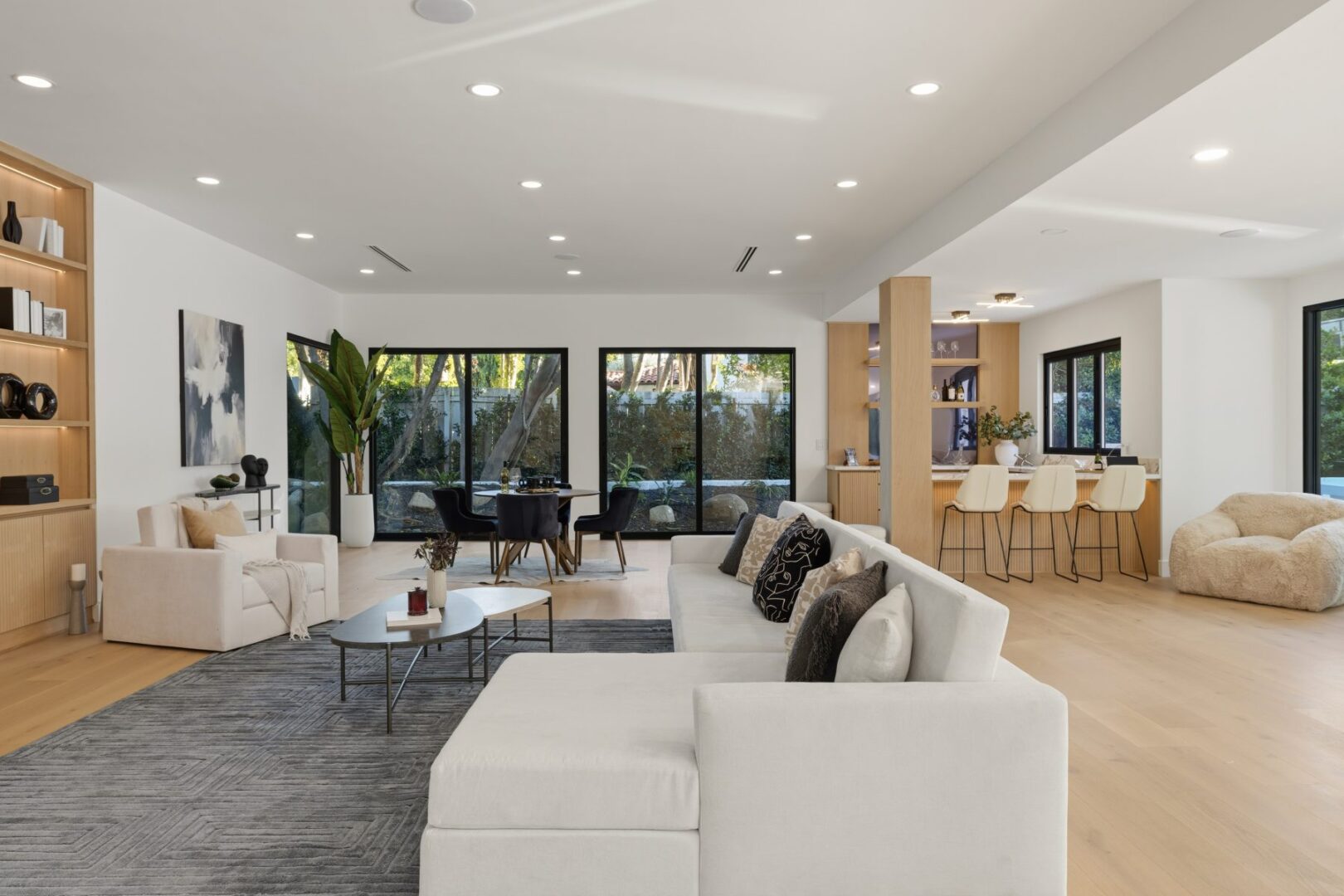 Open great room connects a seating area and dining space to the kitchen and garden-facing glass doors.