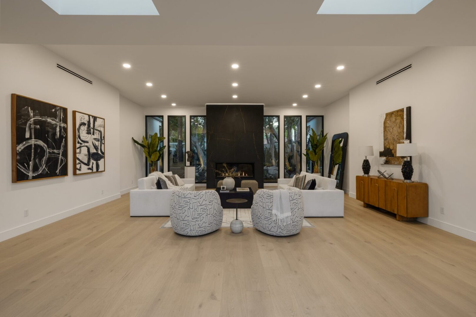 Symmetrical seating surrounds a central fireplace, with tall windows and a wood console along the walls.