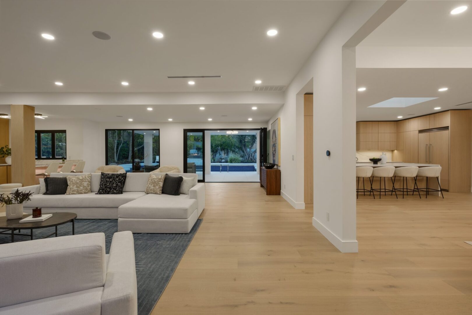 Open great room with sectional seating, pale wood floors, and a view into the kitchen.