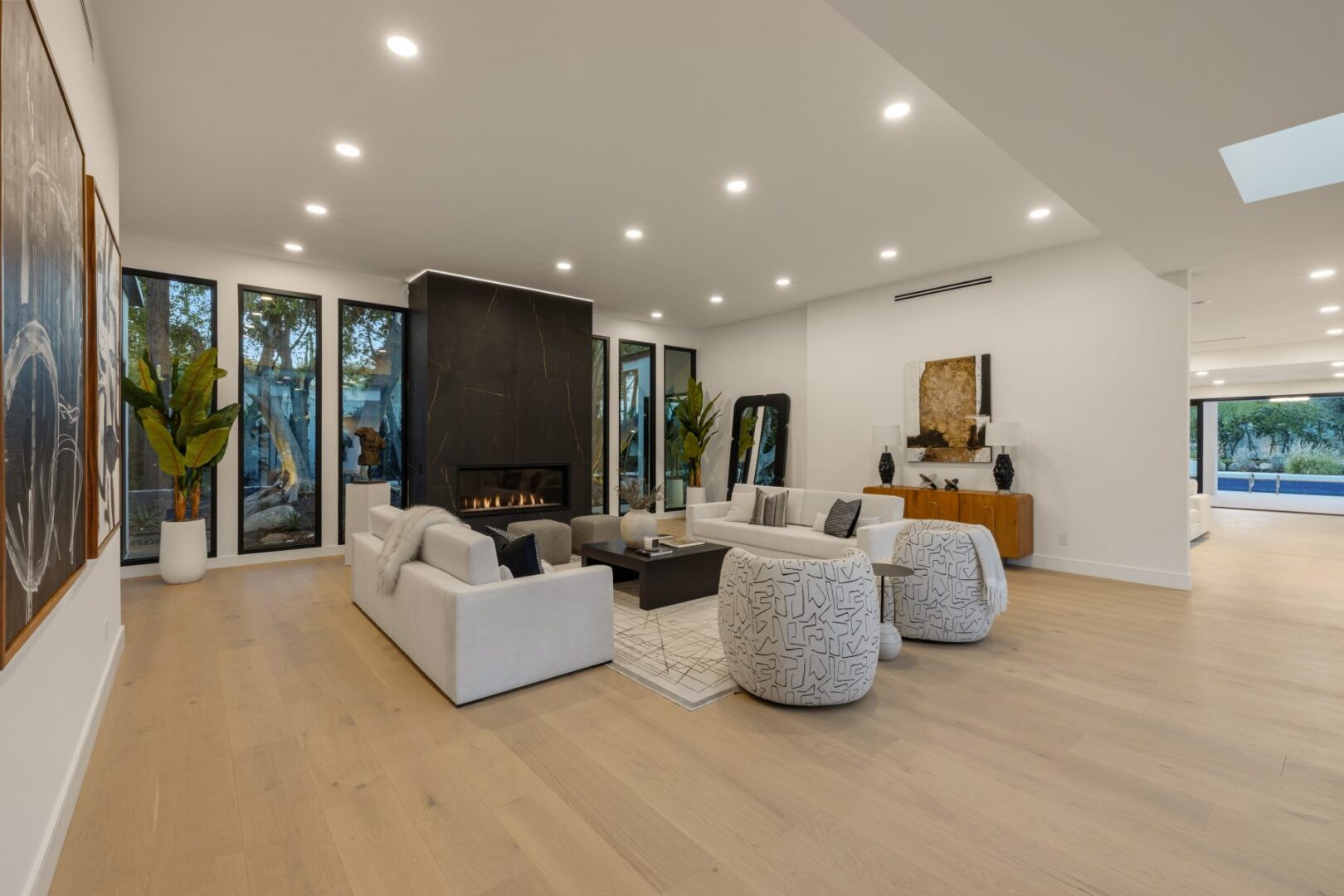 Great room seating faces a fireplace, with broad windows, accent chairs, and a console across the space.