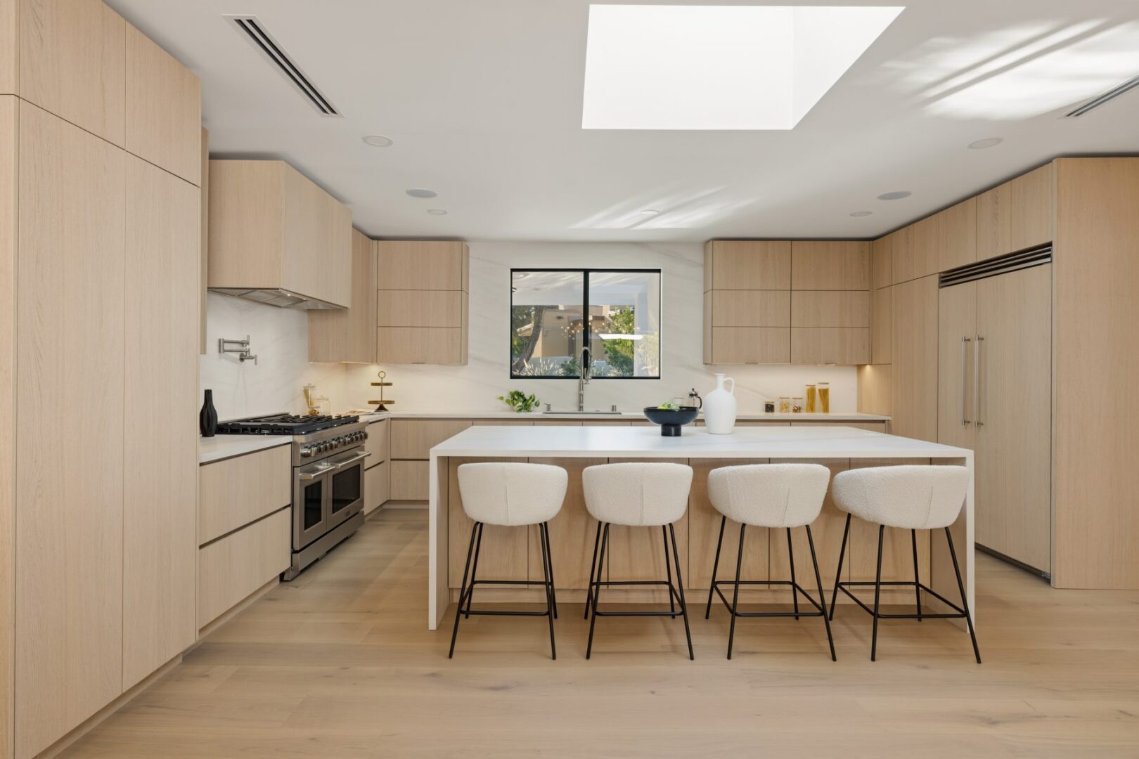 Kitchen with a large island and four stools, wood cabinetry, a range, and a window above the sink.
