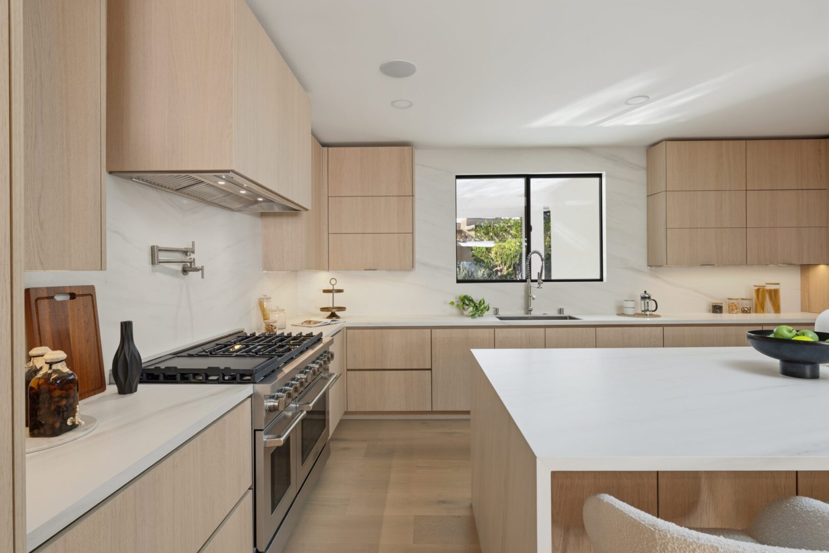 Kitchen work area with a wide island, gas range, wood cabinets, and a sink beneath the window.