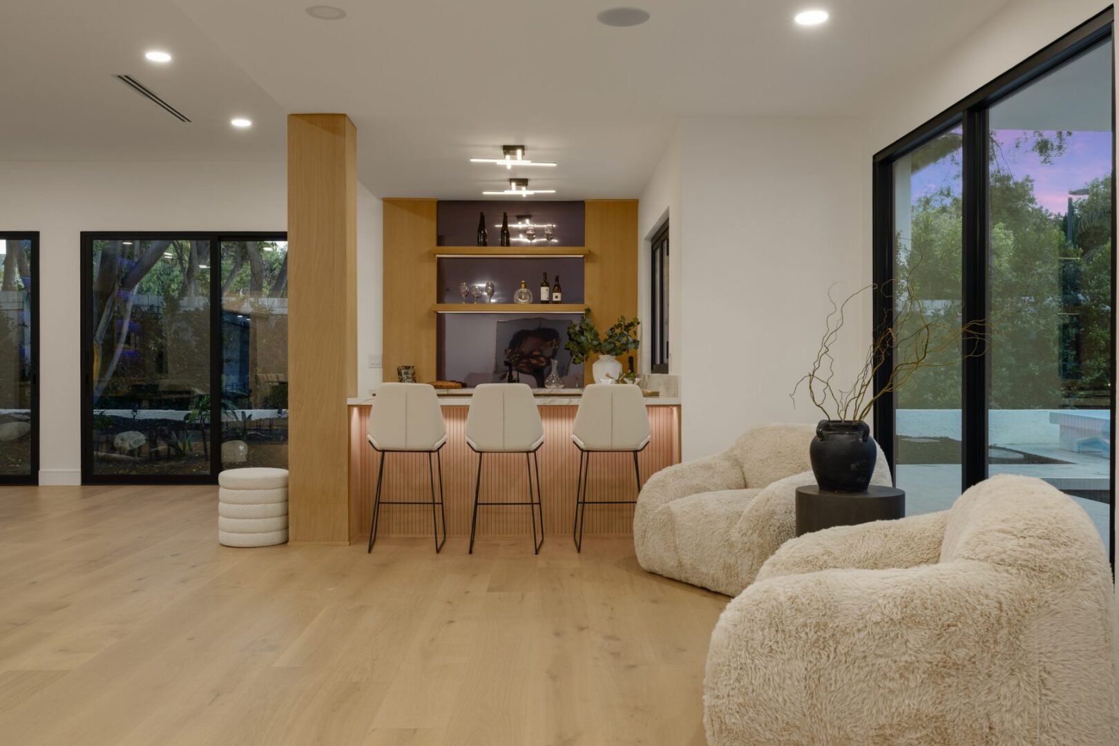 Living area with upholstered lounge chairs beside a bar and large windows opening to the patio.