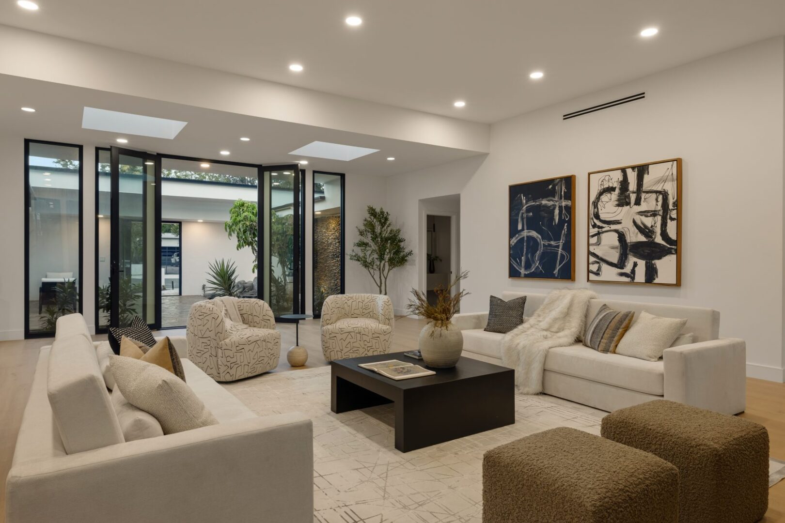 Living area has sofas, patterned chairs, and a central coffee table beside glass doors to the courtyard.