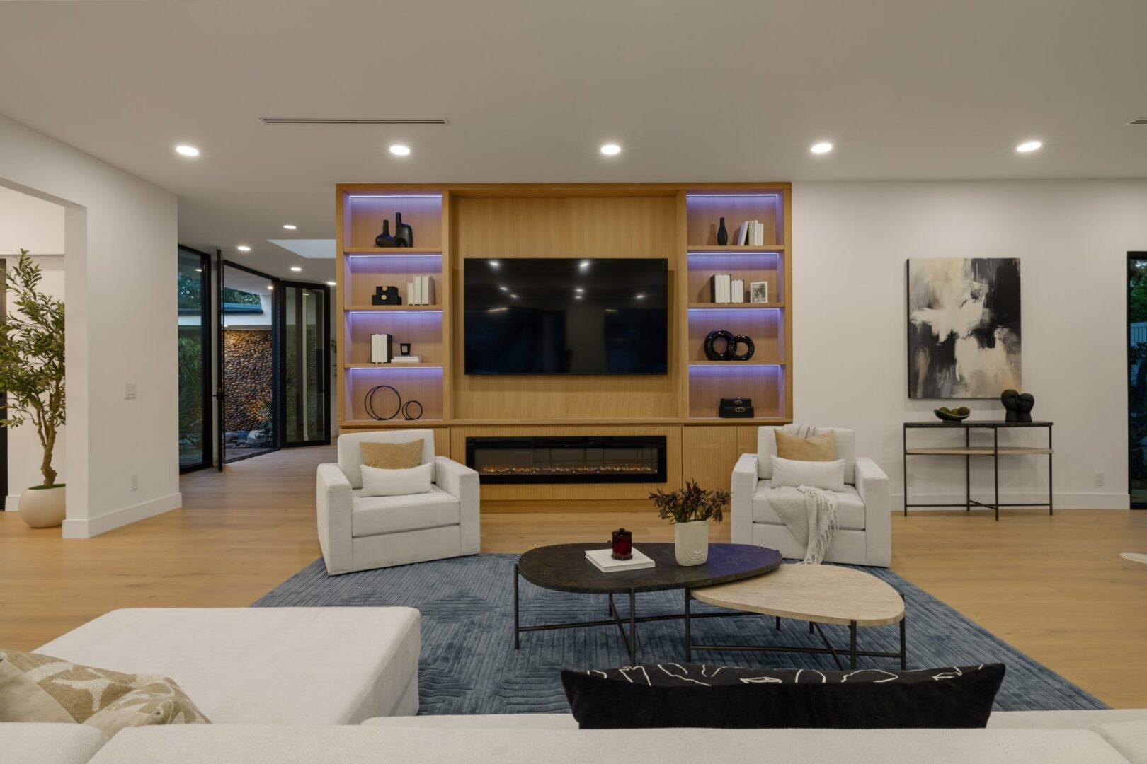 Living room with built-in television wall, linear fireplace, display shelves, and seating around coffee tables.