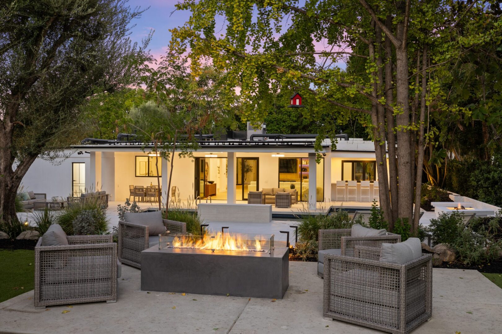 Outdoor lounge with woven chairs and a fire feature faces the home’s glass doors and covered patio.