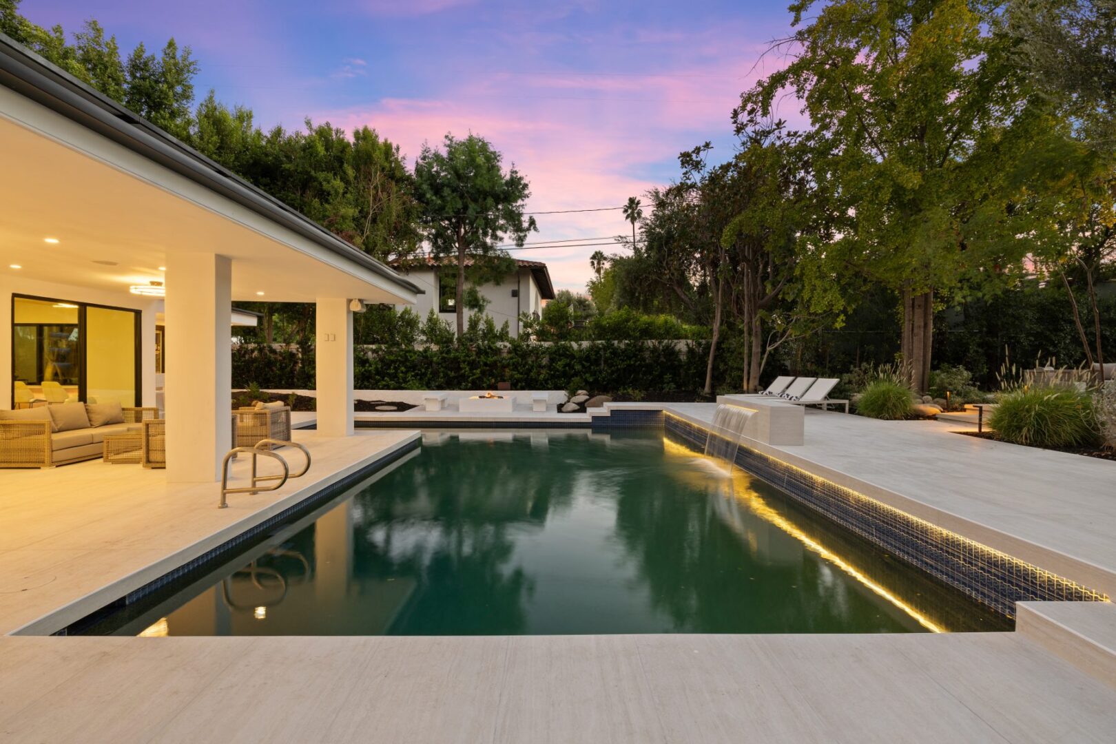 Swimming pool beside a covered seating area, with loungers and a paved patio.