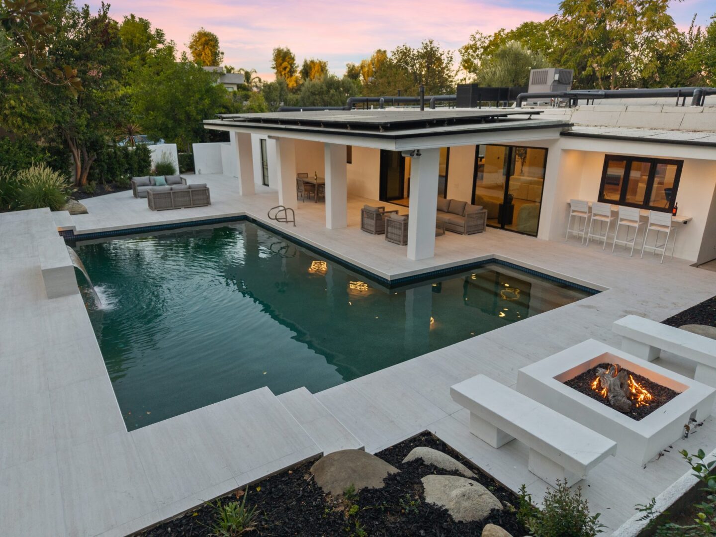 Backyard pool beside a covered patio with outdoor seating, a dining counter, and a built-in fire feature.