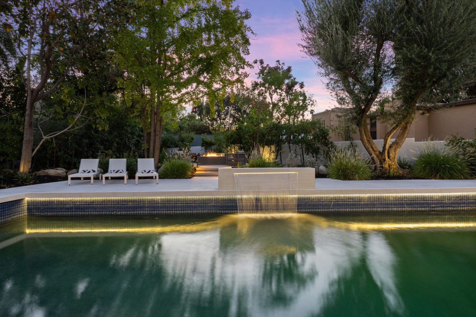 Swimming pool edge with a narrow water spillway faces a landscaped terrace and lounge chairs.