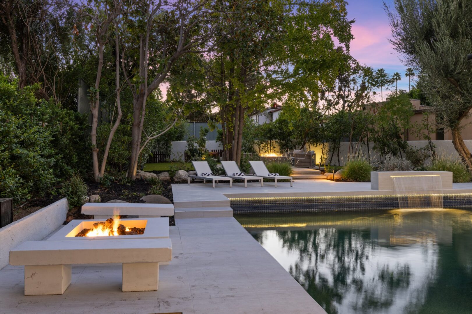 Poolside view across the water to a raised lounge deck with chairs and a built-in fire feature.