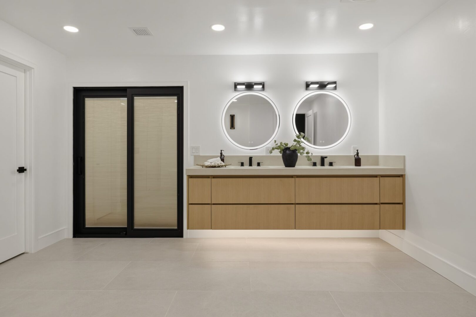 Bathroom vanity with two sinks, round mirrors, wood cabinetry, and a sliding glass door.