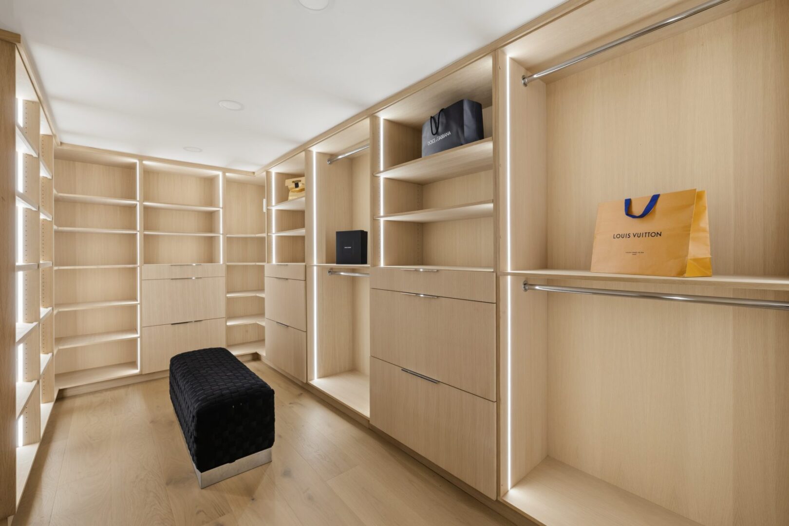 Walk-in closet with pale wood cabinetry, open shelving, hanging rails, drawers, and a central bench.