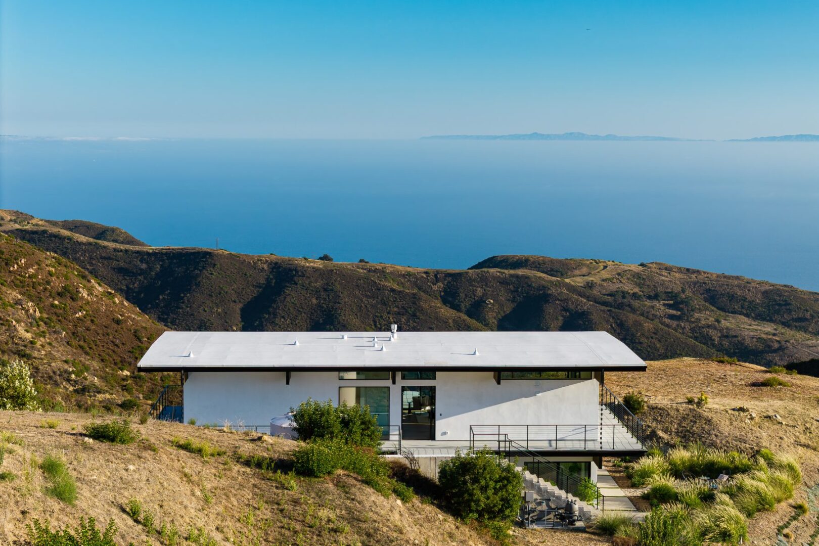 Aerial view of a modern home on a hillside with ocean in the background.