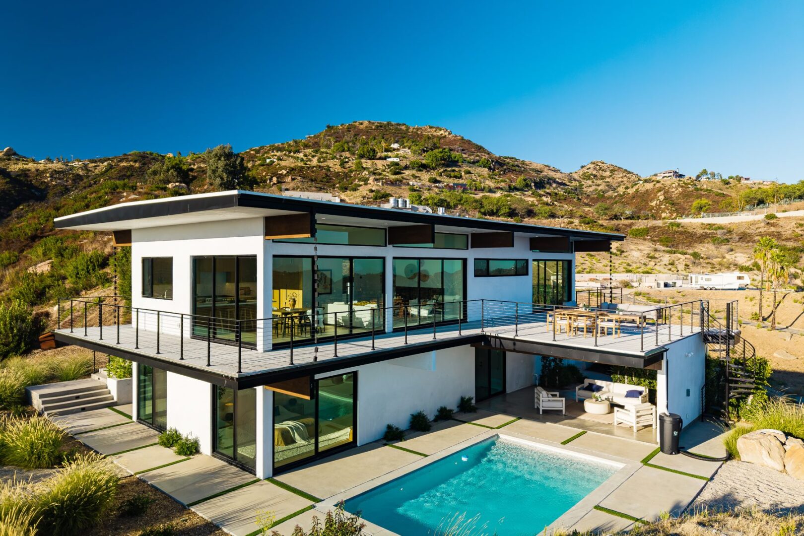 Aerial view of a modern home with pool, surrounded by hills and clear sky.