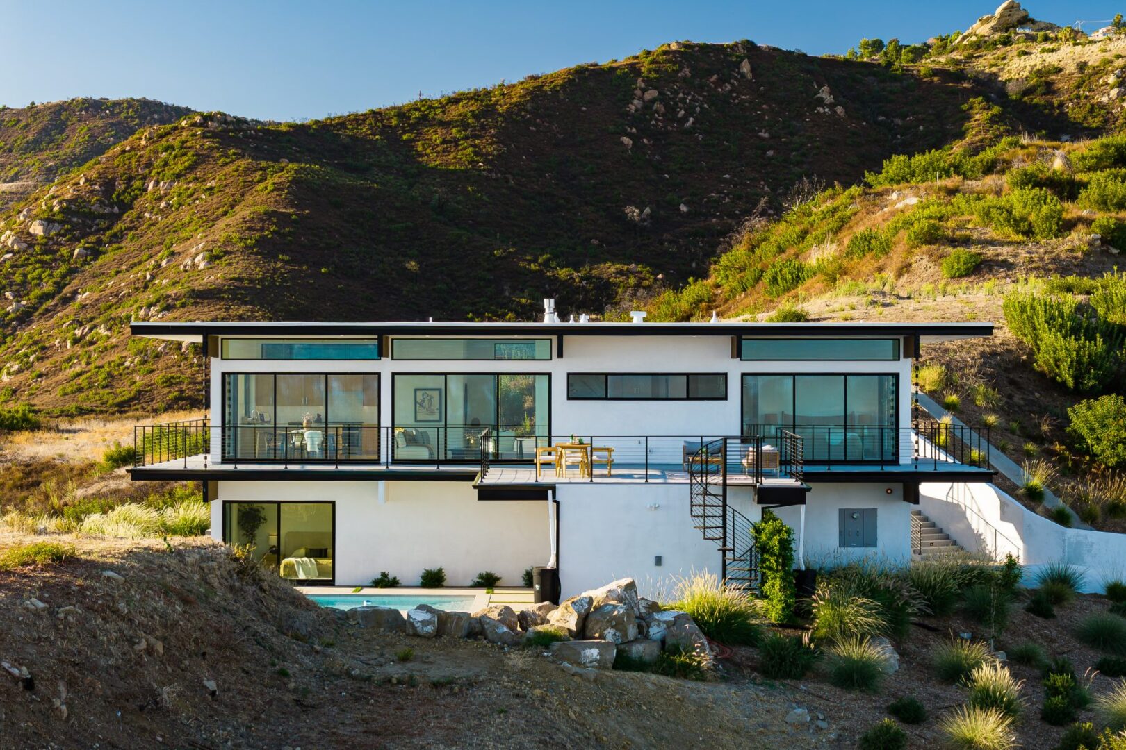 Modern home with large glass windows and mountain backdrop under clear sky.