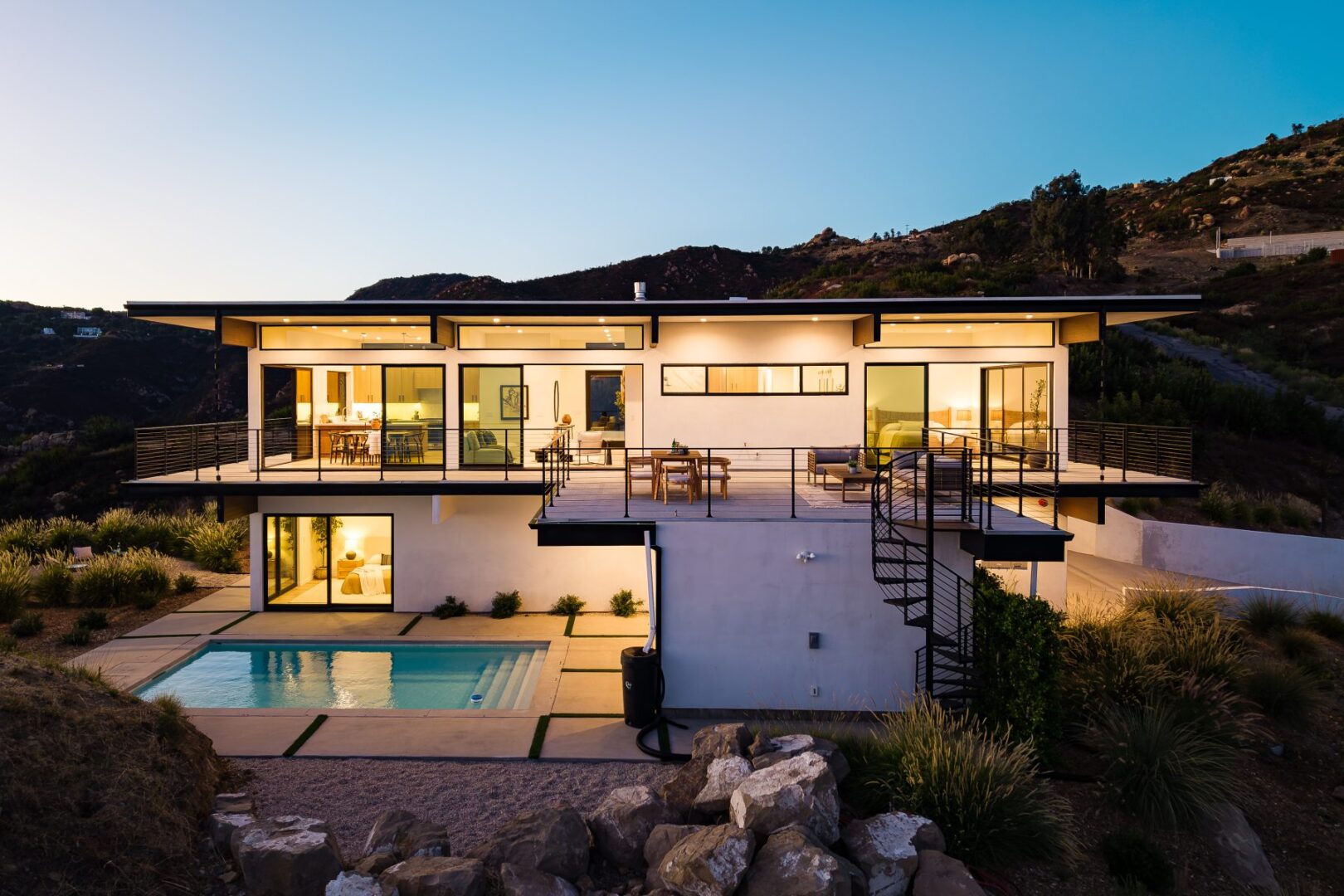 Twilight view of modern home with illuminated interiors and pool.