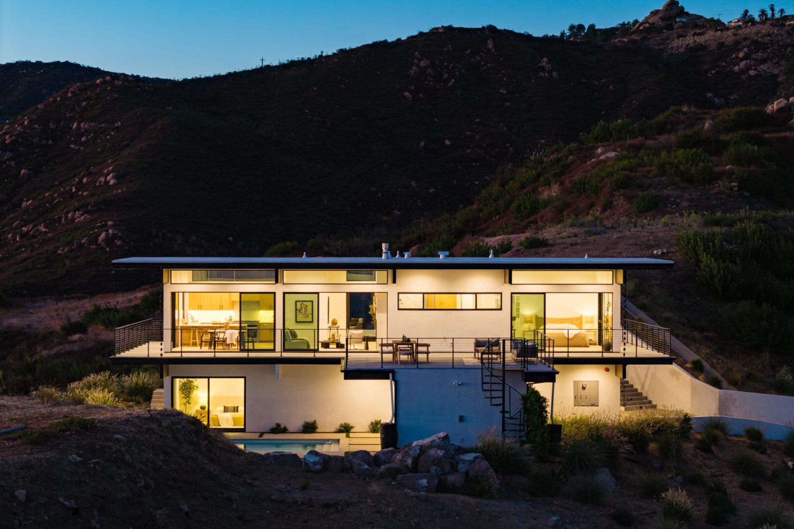 Twilight view of modern home with illuminated windows and pool area.