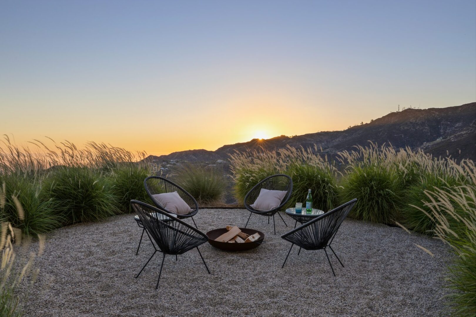 Outdoor seating area with fire pit, overlooking sunset and mountains.