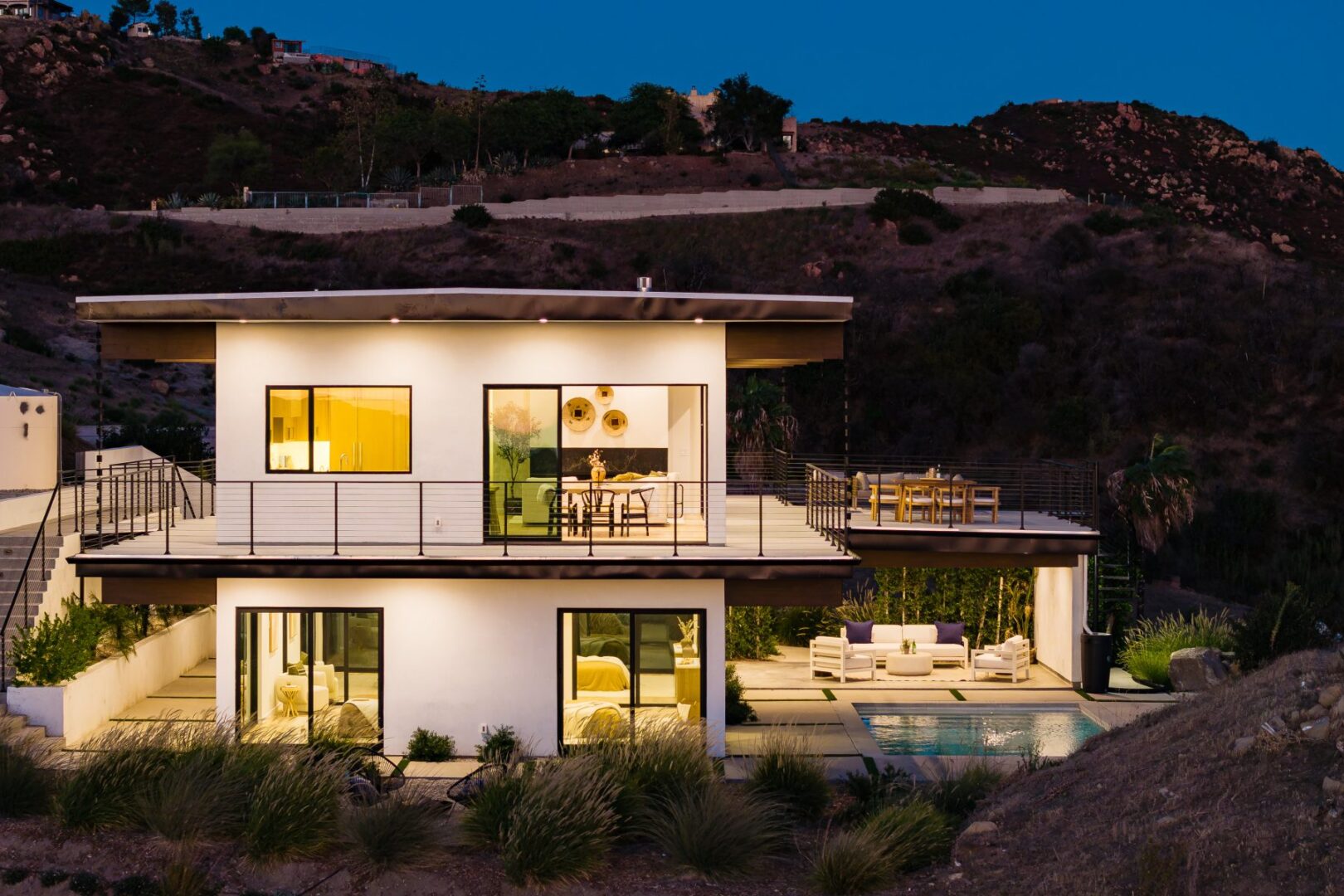 Modern home exterior at twilight with illuminated windows and pool area.