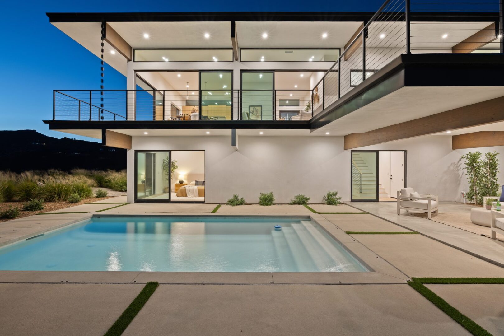 Illuminated pool area of a modern home at night, showcasing interior lights.