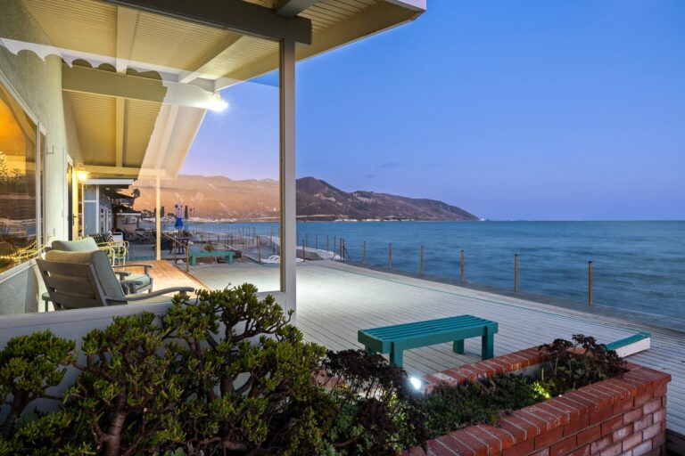 Spacious beachfront deck at dusk with lounge chairs and a stunning view of the ocean and mountains.