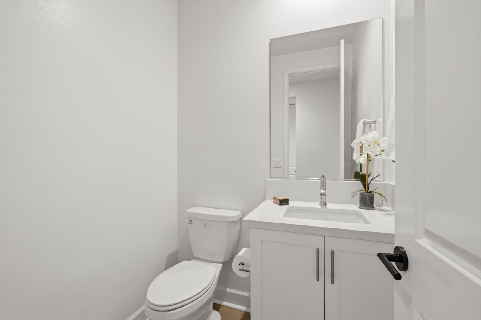 Compact bathroom with a white vanity, mirror, toilet, and an open doorway.