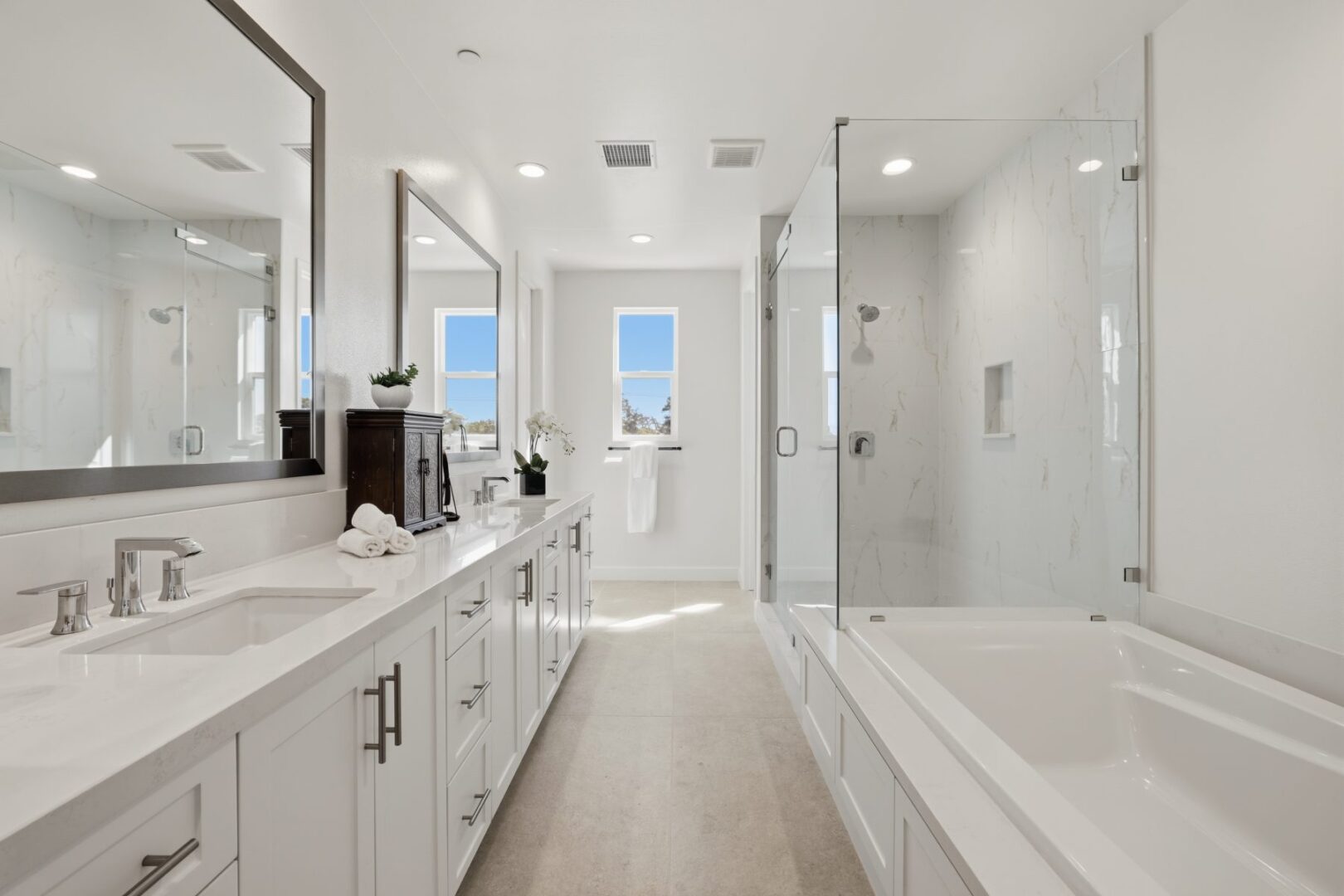 Bathroom with a long double vanity, two windows, and a glass-enclosed shower beside a soaking tub.