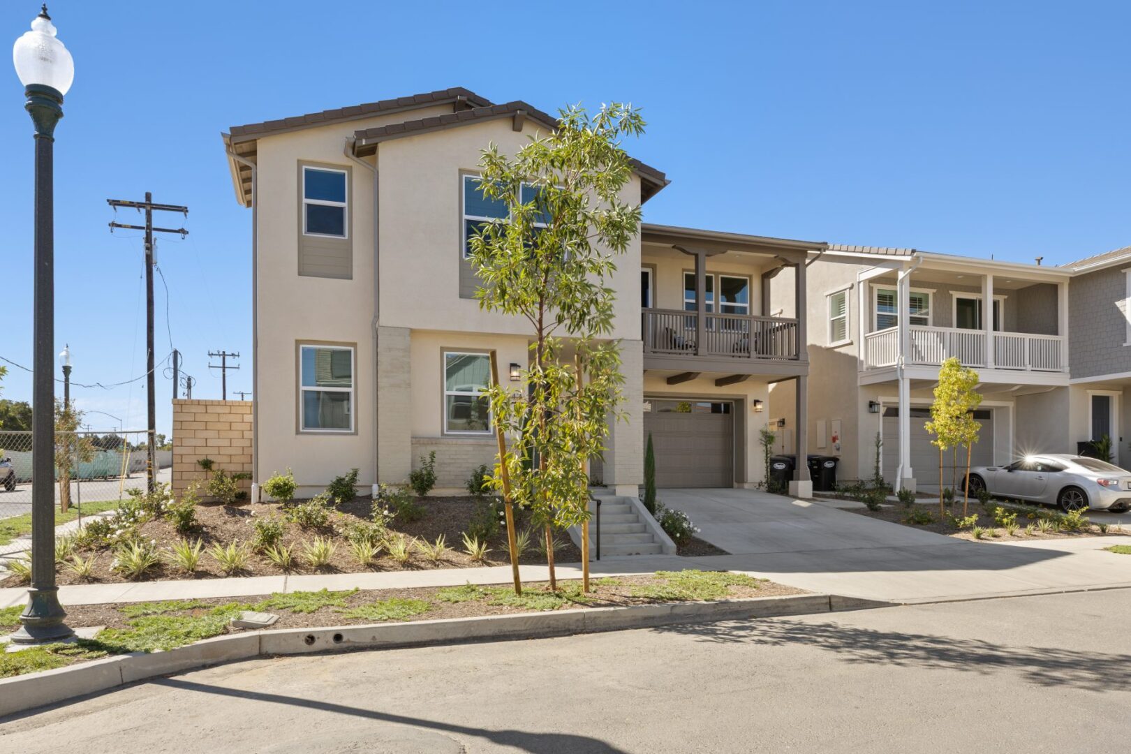 Two-story attached home with a balcony, front garage, planted walkway, and neighboring residences.
