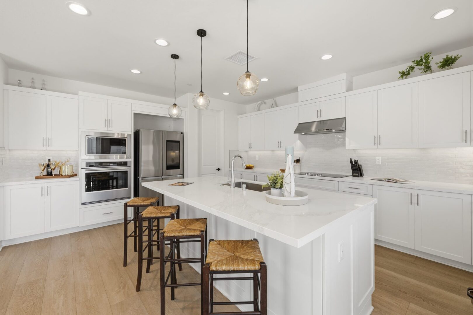 Kitchen with a broad island, bar stools, white cabinetry, built-in ovens, and stainless steel refrigerator.