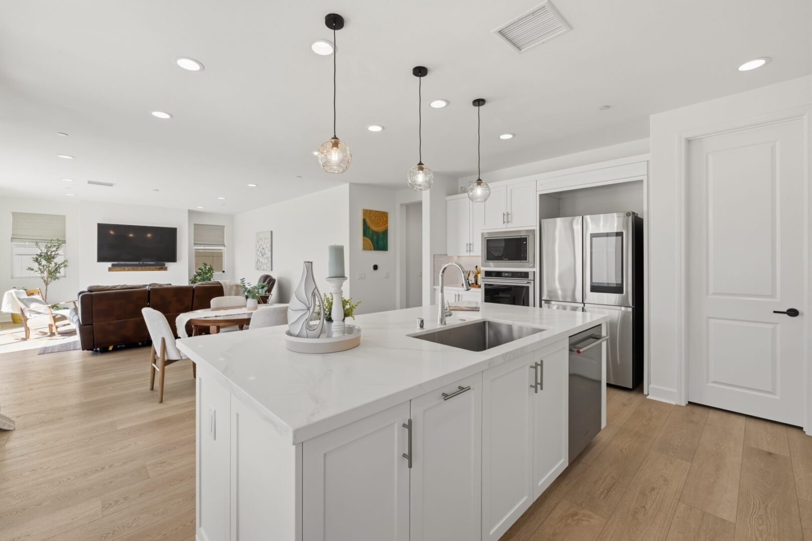 White kitchen island with sink and seating opens to a living area with a fireplace and television.