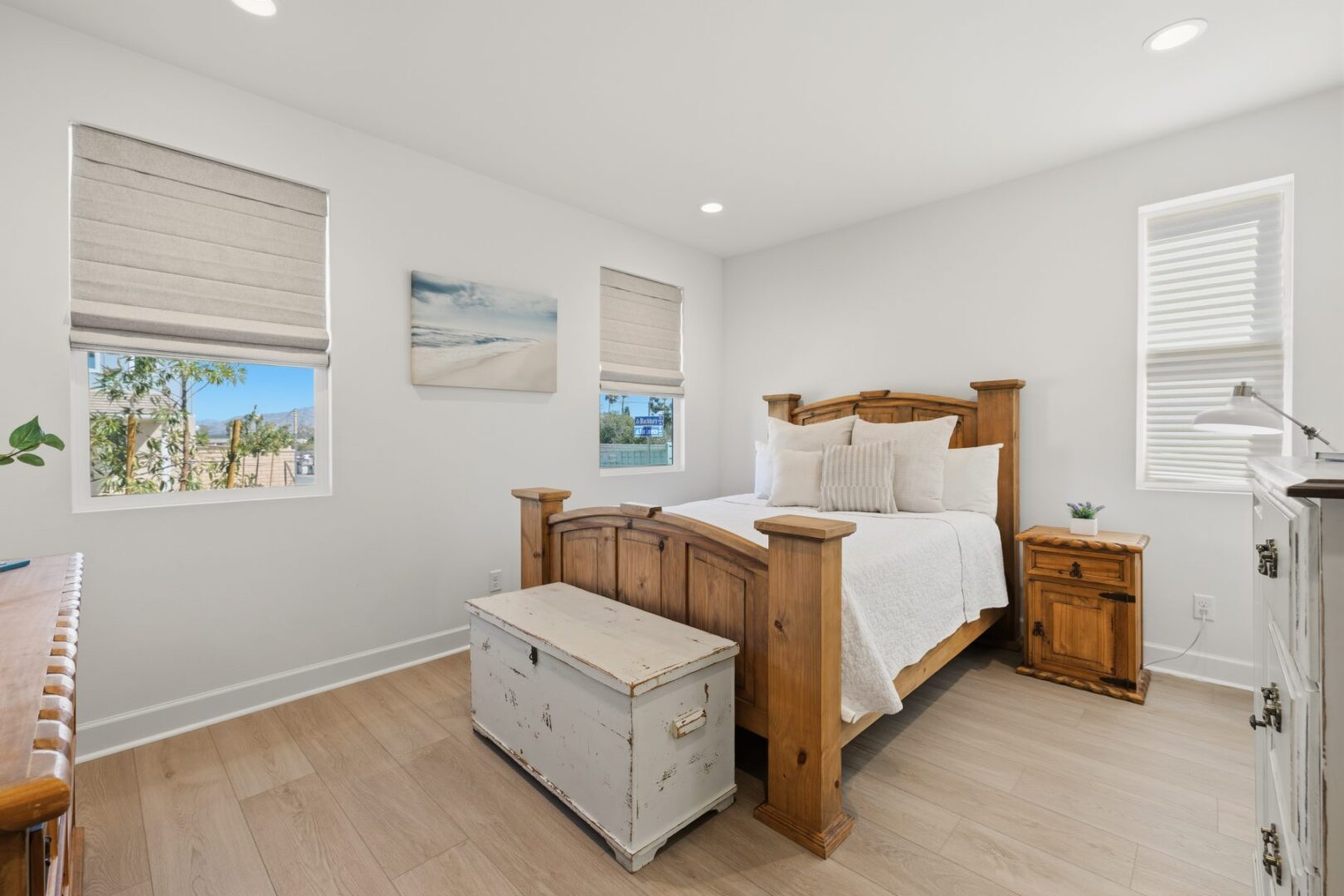Bedroom with a wood four-poster bed, white bedding, bedside table, and windows overlooking nearby homes.