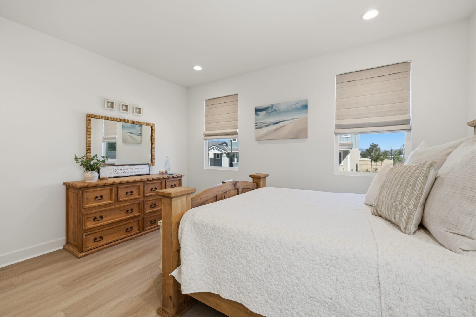 Bedroom with a wood bed and dresser, white bedding, and windows facing neighboring homes.